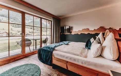 Deluxe Modernes Hotelzimmer mit Holzbett, Alpenblick durch große Fenster und Balkonmöbeln
